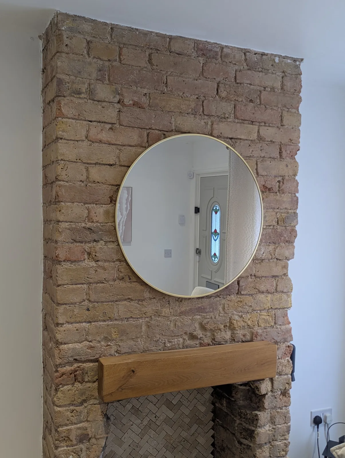 Round gold mirror hung on an exposed brick chimney